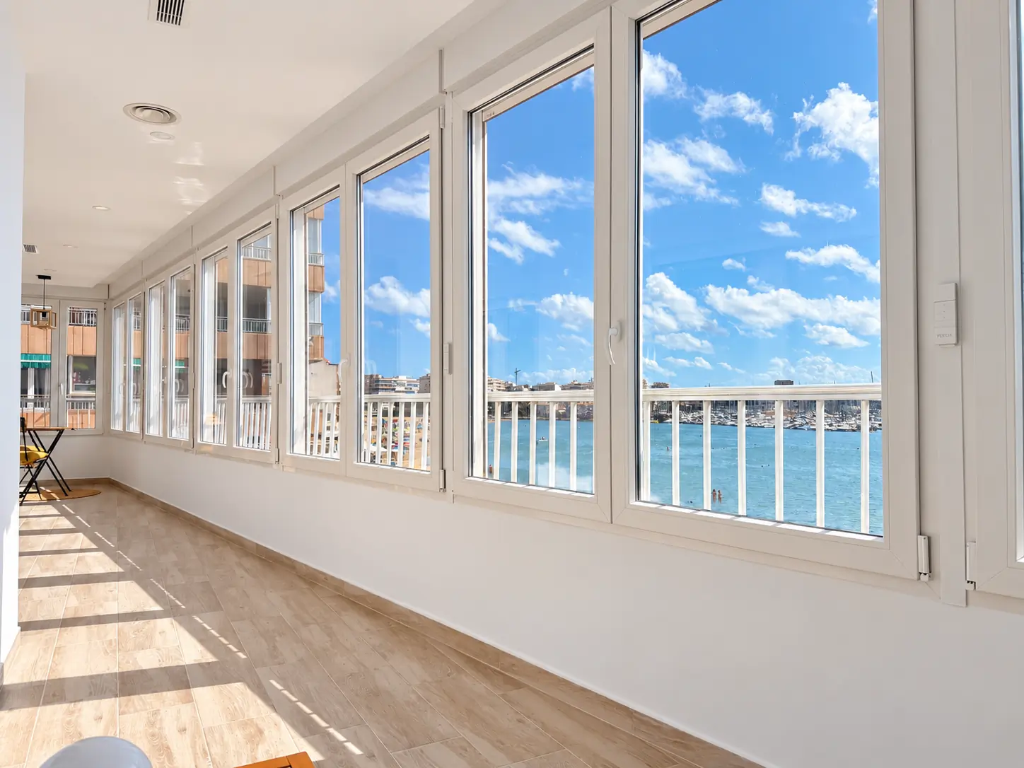 Terrace after renovation &mdash; light porcelain flooring, sleek glass railing and stylish outdoor lounge and dining area with panoramic Mediterranean sea view