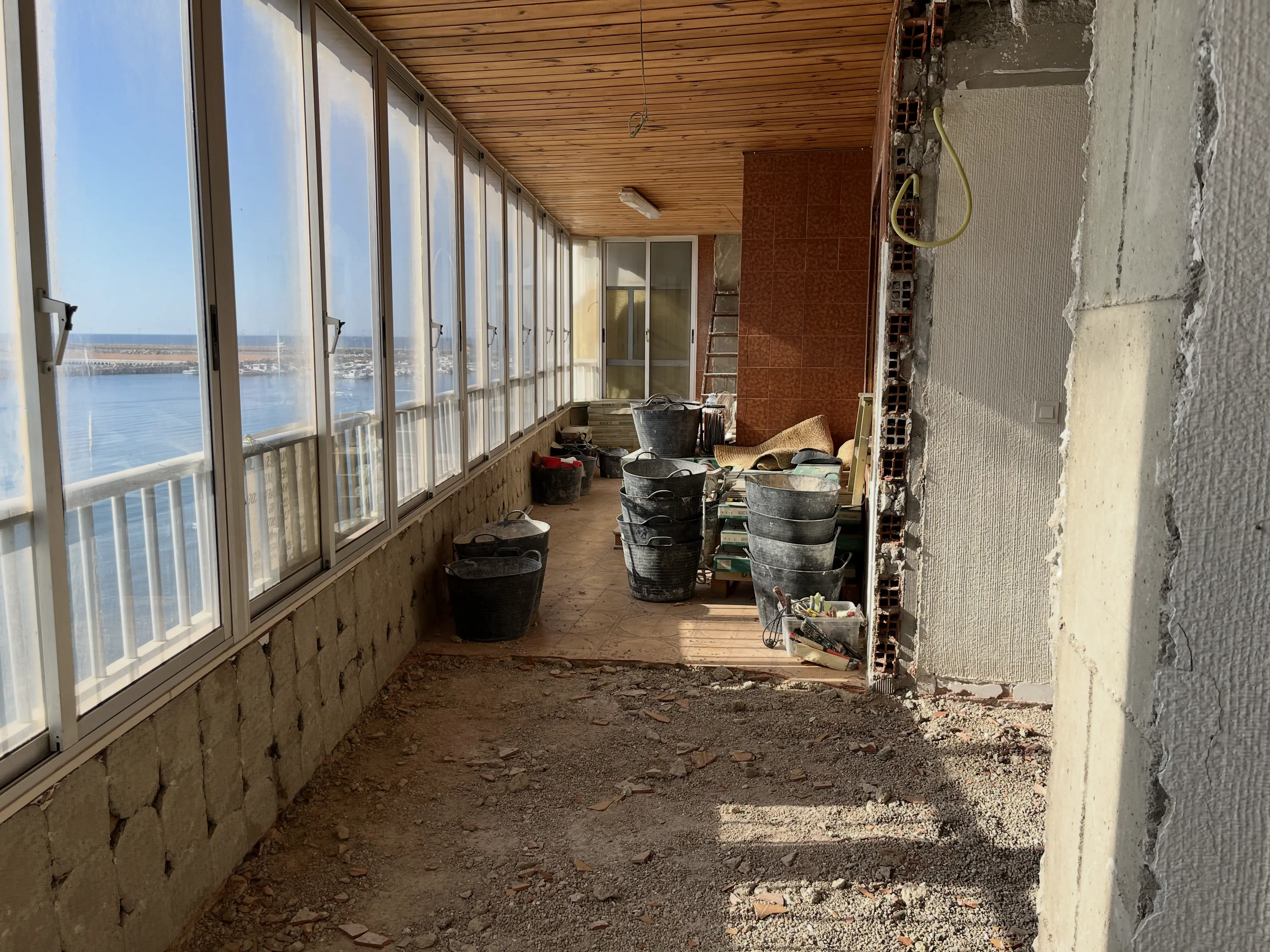 Terrace before renovation &mdash; worn tiled floor, rusty metal railing and faded plastic furniture on a dated Costa Blanca balcony